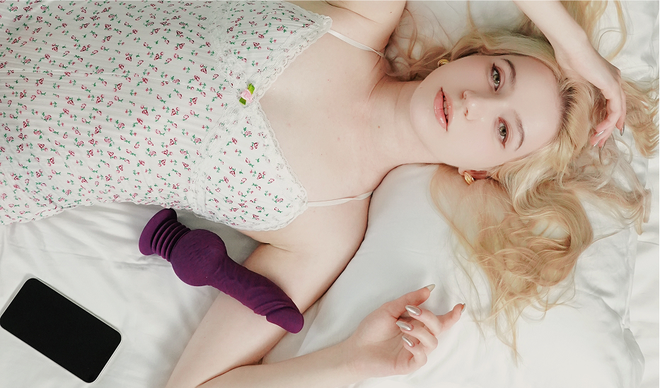 Woman on bed with smartphone and purple silicone vibrator on white sheets