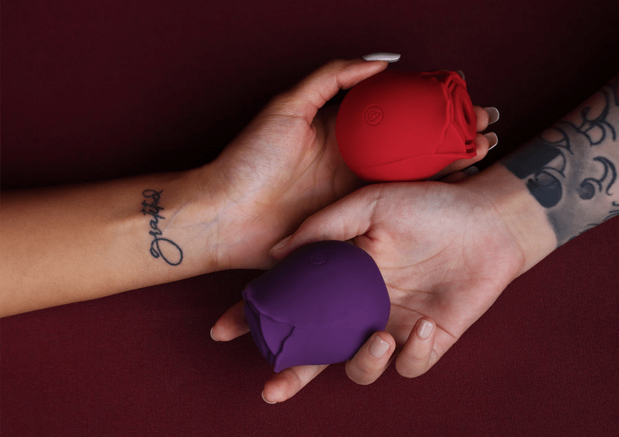 Red and purple rose-shaped adult toys held by two hands, one with Grateful tattoo