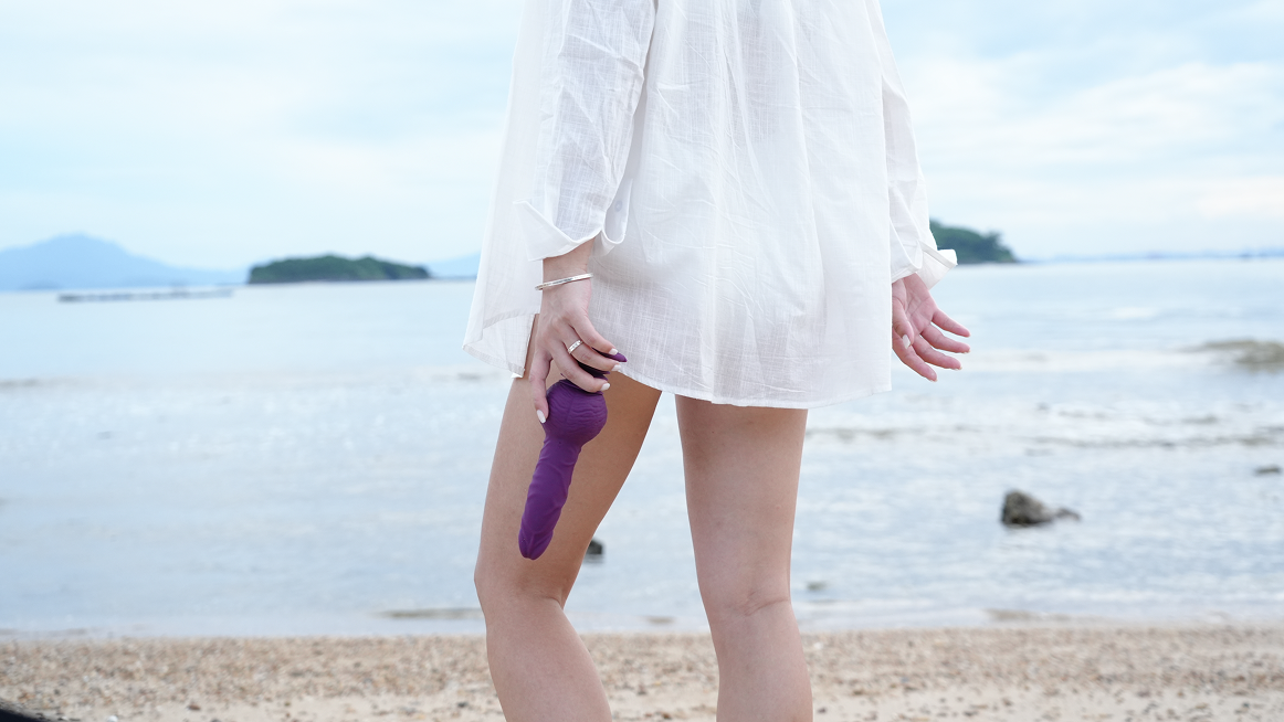 Person holding purple textured dildo on the beach