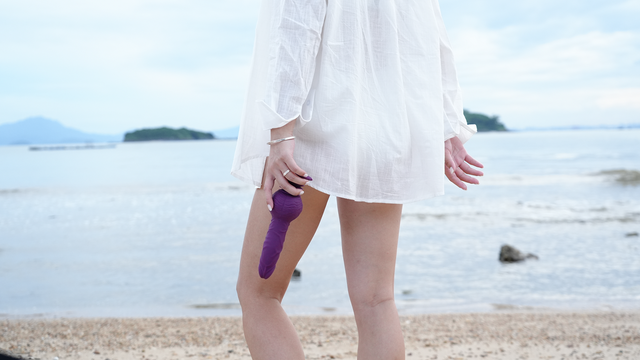 Person holding purple textured dildo on the beach