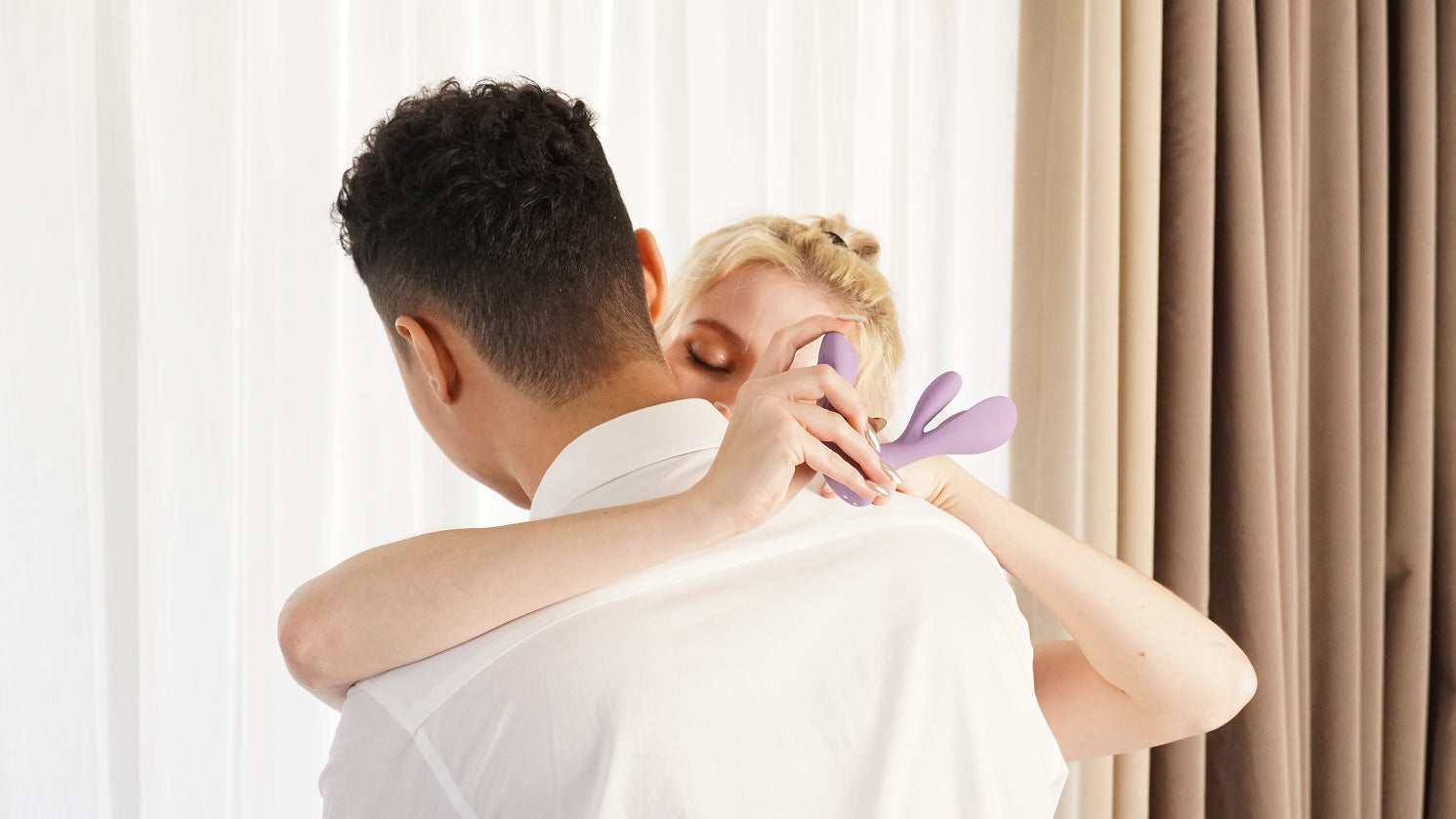 A couple enjoying intimate moments, with the woman holding a purple vibrator behind her partner's back