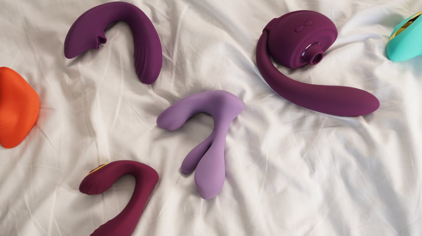 Assorted purple and pink vibrators displayed on white bed