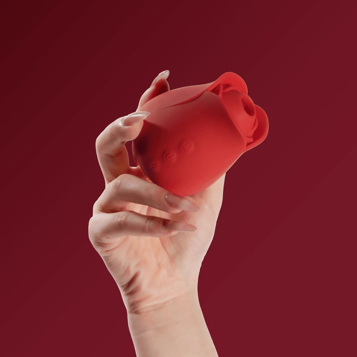 Hand holding red rose-shaped portable clitoral sucker on burgundy background
