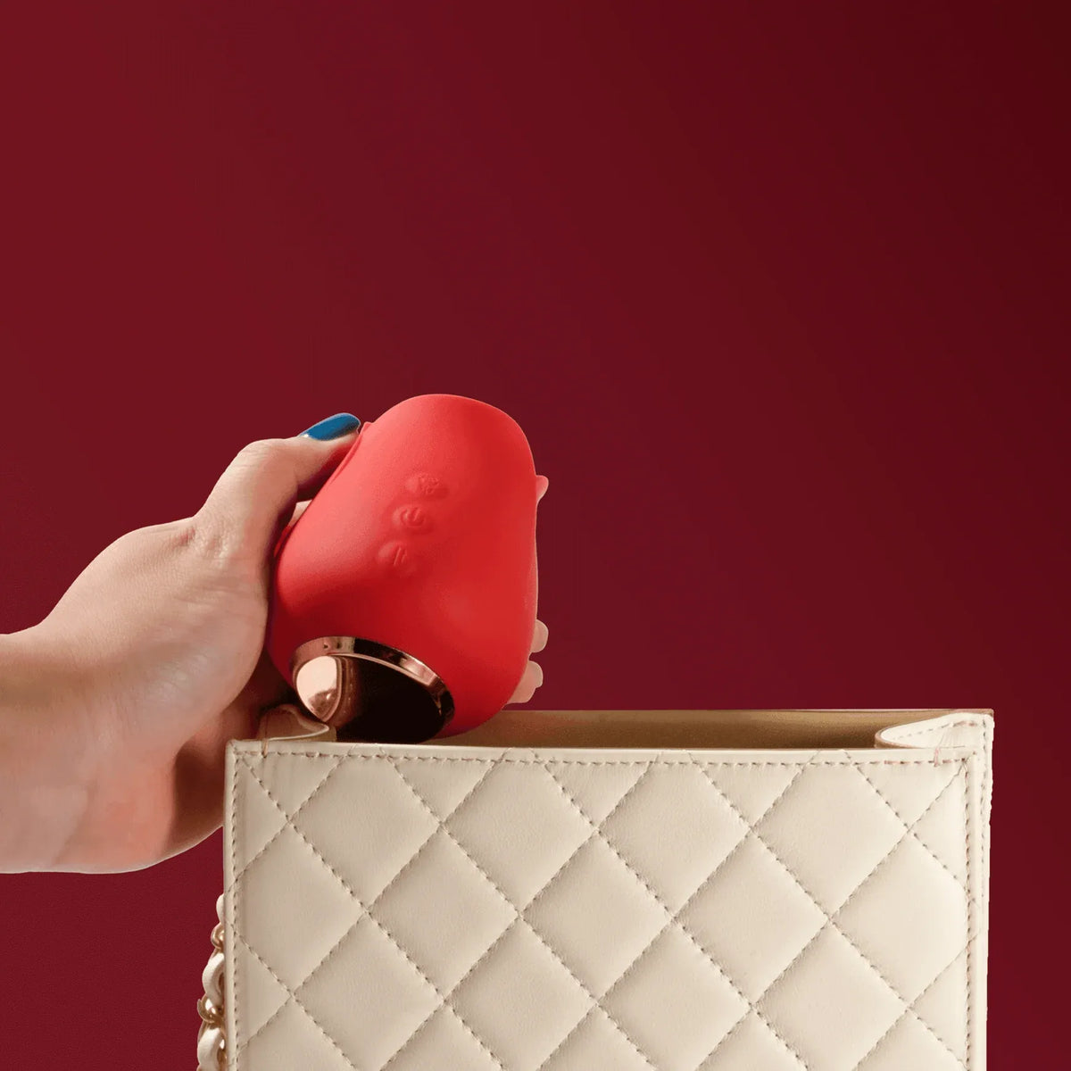 Portable red rose clitoral sucker held above a quilted cream handbag