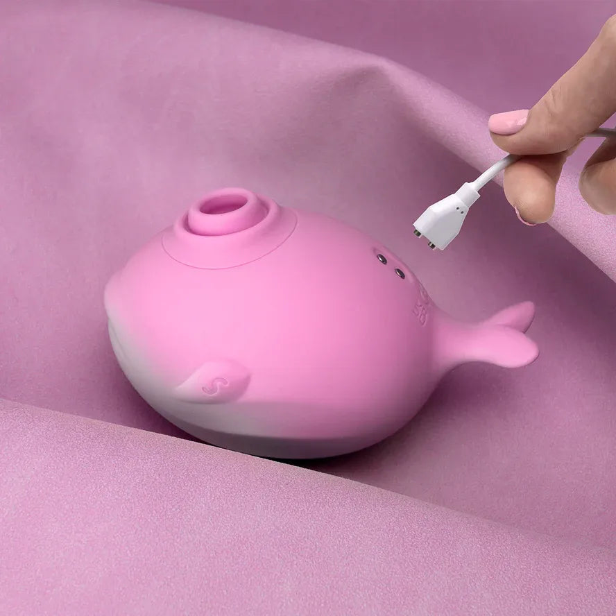 Pink whale-shaped clitoral sucker with USB charging cable on pink background