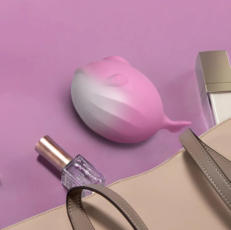 Pink whale-shaped clitoral sucker with smooth silicone finish on purple background