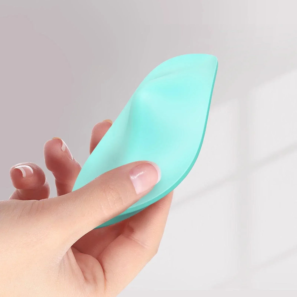 Mint green silicone wearable panty vibrator held in hand, ergonomic curved design